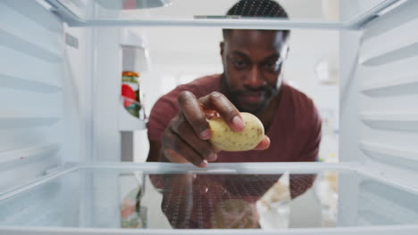 Disappointed-Man-Looking-Inside-Refrigerator-Empty-Except-For-Potato-On-Shelf