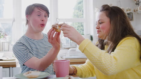 Young-Downs-Syndrome-Couple-Enjoying-Tea-And-Cake-In-Kitchen-At-Home