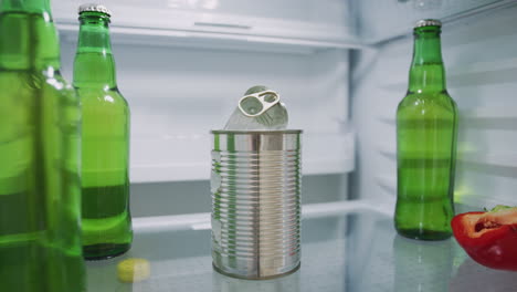 Young-Man-Looking-Inside-Refrigerator-Empty-Except-For-Open-Tin-Can-And-Bottles-Of-Beer-On-Shelf