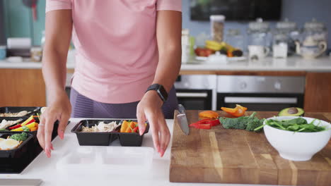 Close-Up-Of-Woman-Wearing-Fitness-Clothing-Preparing-Batch-Of-Healthy-Meals-At-Home-In-Kitchen