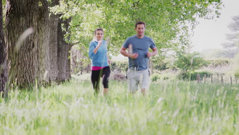 Crane-Shot-Of-Couple-Exercising-Running-Through-Countryside-Field