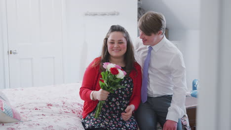 Loving-Young-Downs-Syndrome-Couple-Sitting-On-Bed-With-Man-Giving-Woman-Flowers