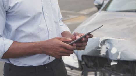 Close-Up-Of-Insurance-Loss-Adjuster-With-Digital-Tablet-Inspecting-Damage-To-Car-From-Motor-Accident