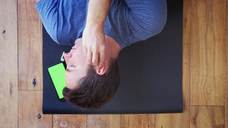 Overhead-View-Of-Man-Lying-On-Exercise-Mat-At-Home-Putting-In-Wireless-Earphones