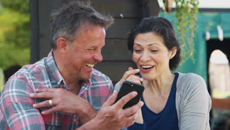 Mature-Couple-In-Garden-Center-Cafe-Looking-At-Pictures-On-Mobile-Phone
