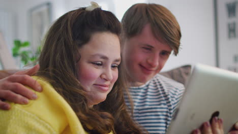 Young-Downs-Syndrome-Couple-Sitting-On-Sofa-Watching-Digital-Tablet-At-Home
