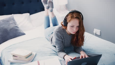 Eine-Studentin-Mit-Kopfhörern-Arbeitet-Mit-Laptop-Und-Mobiltelefon-Im-Gemeinsamen-Haus-Im-Bett