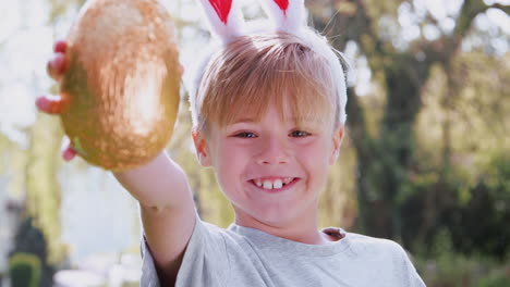 Retrato-De-Un-Niño-Con-Orejas-De-Conejo-Sosteniendo-Un-Huevo-De-Chocolate-En-La-Búsqueda-De-Huevos-De-Pascua-En-El-Jardín