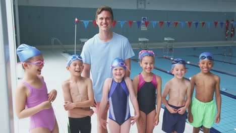 Portrait-Of-Children-Standing-By-Edge-Of-Swimming-Pool-With-Male-Coach-For-Lesson