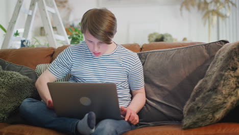 Junger-Mann-Mit-Down-Syndrom-Sitzt-Zu-Hause-Auf-Dem-Sofa-Und-Benutzt-Einen-Laptop