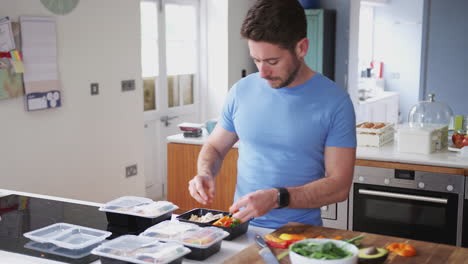 Man-Wearing-Fitness-Clothing-Preparing-Batch-Of-Healthy-Meals-At-Home-In-Kitchen