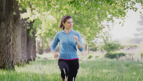 Crane-Shot-Of-Woman-Exercising-Running-Through-Countryside-Field