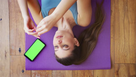 Overhead-View-Of-Woman-Lying-On-Exercise-Mat-At-Home-Putting-In-Wireless-Earphones