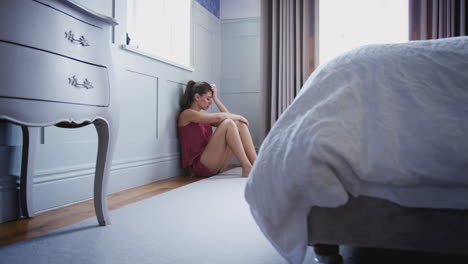 Depressed-Woman-Wearing-Pajamas-Sitting-On-Floor-Of-Bedroom