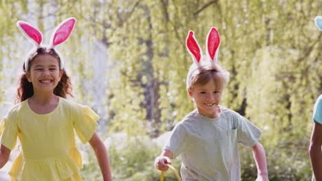 Group-Of-Children-Wearing-Bunny-Ears-Running-On-Easter-Egg-Hunt-In-Garden