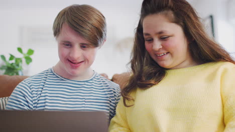 Young-Downs-Syndrome-Couple-Sitting-On-Sofa-Using-Laptop-At-Home