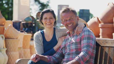 Portrait-Of-Mature-Couple-Sitting-On-Bench-Whilst-Visiting-Garden-Center