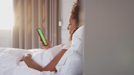 Woman-Sitting-Up-In-Bed-Looking-At-Mobile-Phone-After-Having-Woken-Up