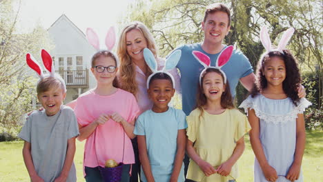 Portrait-Of-Parents-And-Children-Wearing-Bunny-Ears-On-Easter-Egg-Hunt-In-Garden