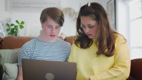 Young-Downs-Syndrome-Couple-Sitting-On-Sofa-Using-Laptop-At-Home
