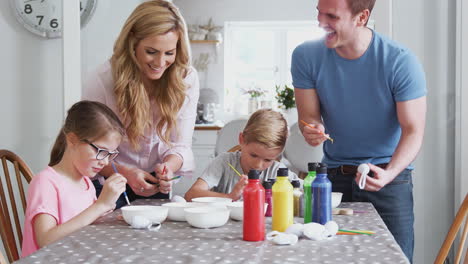 Parents-With-Children-Sitting-At-Table-Decorating-Eggs-For-Easter-At-Home