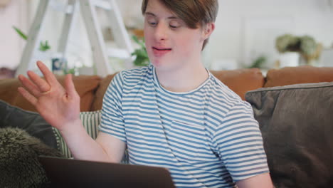Young-Downs-Syndrome-Man-Sitting-On-Sofa-Watching-Laptop-At-Home-And-Dancing