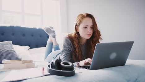 Female-College-Student-Works-On-Bed-In-Shared-House-With-Laptop