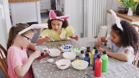 Group-Of-Girls-Wearing-Bunny-Ears-Sitting-At-Table-Decorating-Eggs-For-Easter-At-Home