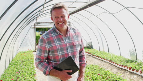 Portrait-Of-Mature-Male-Owner-Of-Garden-Center-Holding-Digital-Tablet-In-Greenhouse