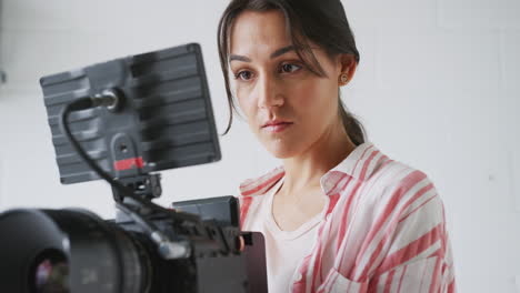 Camarógrafo-Femenino-Con-Cámara-De-Vídeo-Filmando-Una-Película-En-Un-Estudio-Blanco