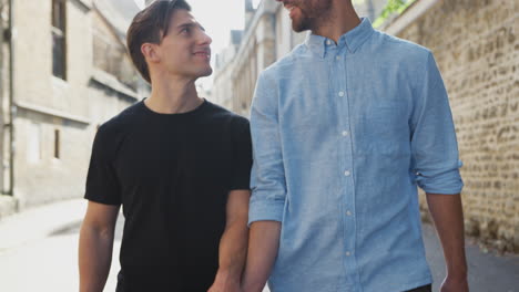 Loving-Male-Gay-Couple-Holding-Hands-Walking-Along-City-Street
