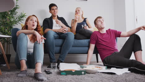 Grupo-De-Estudiantes-Universitarios-En-Casa-Compartida-Viendo-Televisión-Y-Comiendo-Pizza