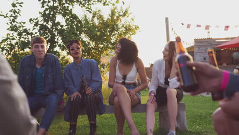 Group-Of-Young-Friends-At-Music-Festival-Sitting-Around-Fire-And-Drinking-Beer