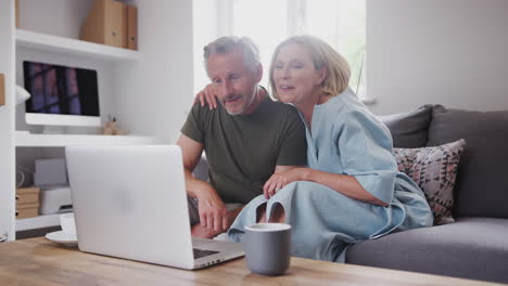 Älteres-Paar-Sitzt-Zu-Hause-Auf-Dem-Sofa-Und-Führt-Gemeinsam-Videoanrufe-Mit-Einem-Laptop-Durch