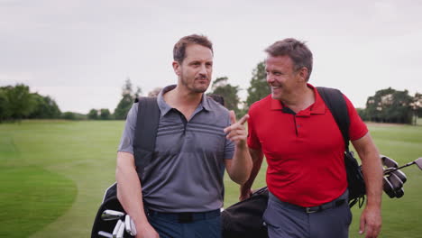 Two-Mature-Couples-Playing-Golf-Walking-Along-Fairway-Carrying-Golf-Bag