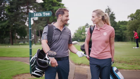Mature-Couple-Playing-Golf-Carrying-Golf-Bag-And-Talking