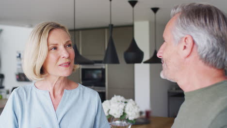 Senior-Couple-Standing-In-Kitchen-And-Talking-Whilst-Drinking-Coffee