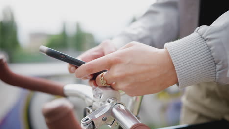 Cerca-De-Una-Mujer-En-Bicicleta-Enviando-Mensajes-De-Texto-Por-Teléfono-Móvil-En-El-Parque-De-Patinaje
