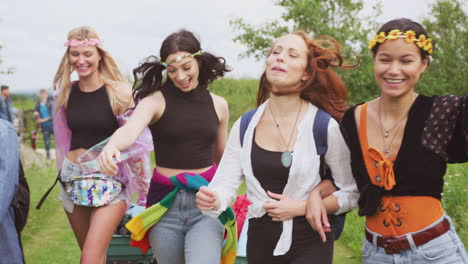 Group-Of-Excited-Young-Female-Friends-Carrying-Camping-Equipment-Through-Field-To-Music-Festival