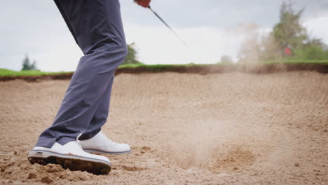 Close-Up-Of-Male-Golfer-Hitting-Golf-Ball-Out-Of-Bunker-And-Onto-Green