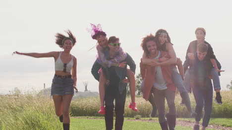 Group-Of-Young-Friends-Giving-Each-Other-Piggyback-Rides-As-They-Walk-Through-Music-Festival-Site