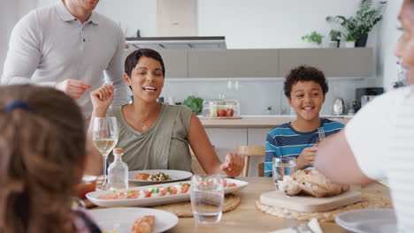 Familia-De-Raza-Mixta-Multigeneracional-Comiendo-Comida-Alrededor-De-La-Mesa-En-Casa-Juntos