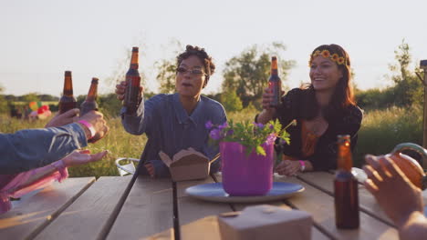 Group-Of-Young-Friends-At-Music-Festival-Sitting-Around-Table-And-Drinking-Beer
