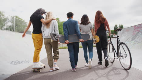 Rear-View-Of-Female-Friends-With-Skateboards-And-Bike-Walking-Through-Urban-Skate-Park