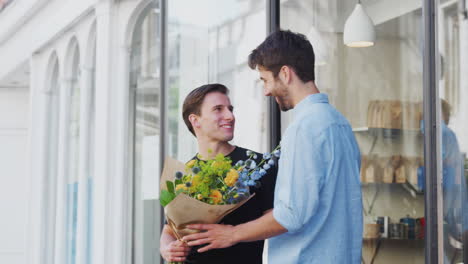 Liebevolles-Männliches-Schwules-Paar,-Das-Händchen-Hält-Und-Aus-Einem-Floristen-Kommt,-Der-Einen-Blumenstrauß-Hält