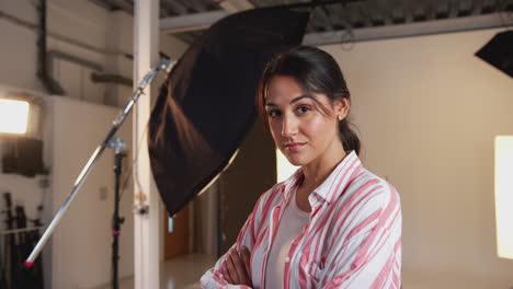 Portrait-Of-Professional-Female-Photographer-Standing-In-Studio-With-Lighting-Equipment