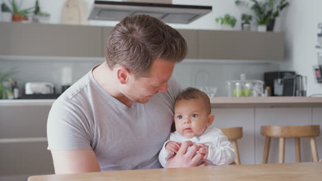 Loving-Father-Holding-3-Month-Old-Baby-Daughter-In-Kitchen-At-Home-Playing-Game