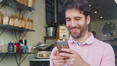 Young-Man-In-Coffee-Shop-Looking-At-Mobile-Phone