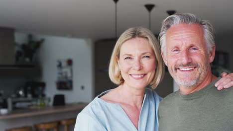Portrait-Of-Smiling-Senior-Couple-Standing-In-Kitchen-Together