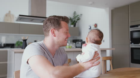 Loving-Father-Holding-3-Month-Old-Baby-Daughter-In-Kitchen-At-Home-Playing-Game